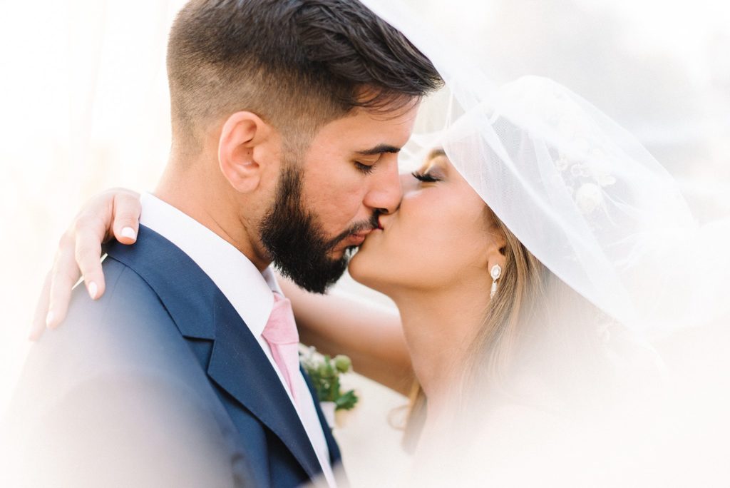 bride and groom under veil kissing